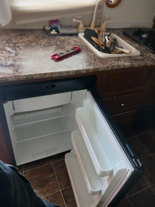 RV rental kitchen featuring a compact open fridge, countertop, sink with utensils, and stovetop. A level tool rests on the counter.. Keystone RV Hideout LHS 2015