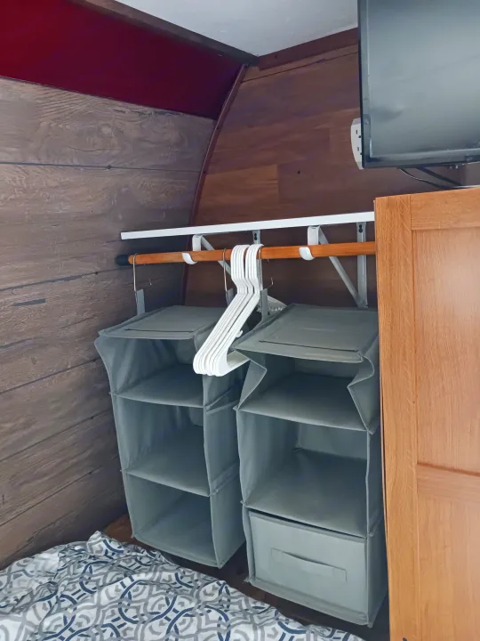 RV rental interior: efficient storage featuring hanging fabric shelves, a clothes rod, and a TV above a bed area.. Keystone RV Hideout LHS 2015
