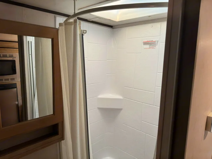 RV rental: A bright white shower stall with a curved curtain rod and skylight is central, with a mirrored cabinet and kitchen on the left.. Forest River RPod 189 2019