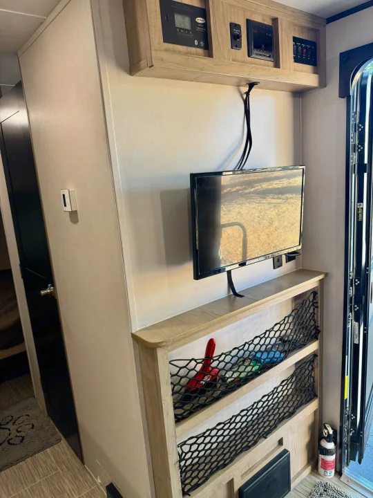 RV rental interior: control panel, wall-mounted TV, netted storage, and a First Alert fire extinguisher by the door.. Forest River RPod 189 2019