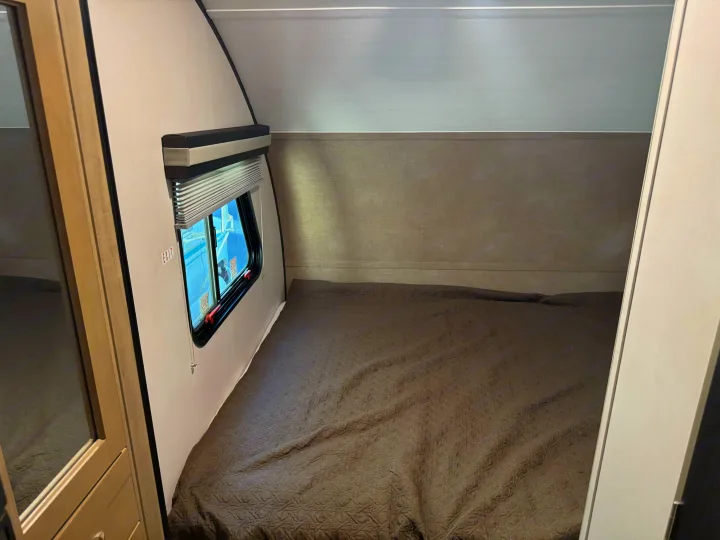 Cozy RV rental bedroom featuring a patterned bed, window with shade, and emergency exit.. Forest River RPod 189 2019