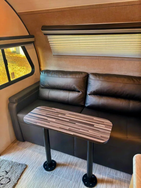 An RV rental interior with a black leather sofa, striped dining table, and windows with blinds.. Forest River RPod 189 2019