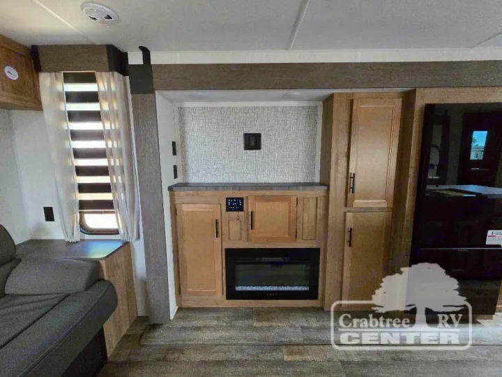 Modern RV rental living space featuring a built-in fireplace, rich cabinetry, and a cozy sofa for travel comfort.. Forest River Cherokee M-274WK 2024