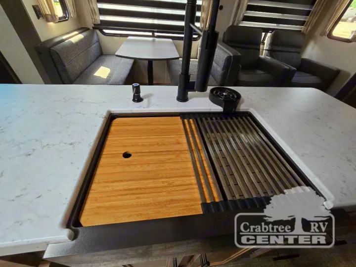 Modern RV rental interior with a bright kitchen counter, large sink, cutting board, dinette, and comfy recliners.. Forest River Cherokee M-274WK 2024
