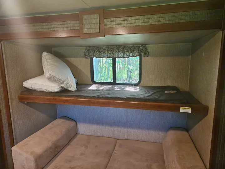 RV rental interior featuring bunk beds with pillows, a lower sofa, and a window overlooking nature.. Keystone RV Passport Grand Touring 2016