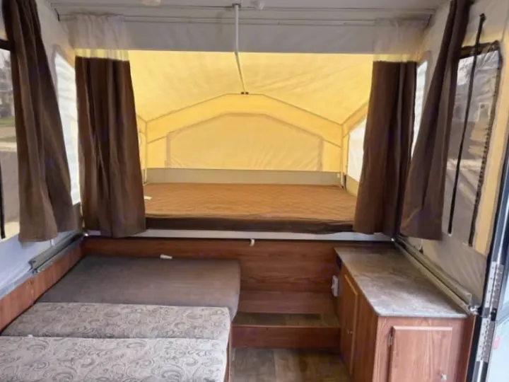 Inside a pop-up RV rental: a bed with brown mattress, patterned bench seating, and wood cabinetry on the right.. Rock wood 1940 LTD 2016