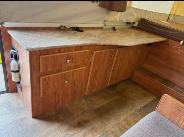 RV rental interior with compact kitchen setup: wood cabinets, speckled countertop, and wood-look flooring. Fire extinguisher visible.. Rock wood 1940 LTD 2016