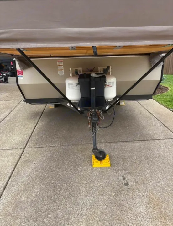 RV rental pop-up camper's front hitch with propane tanks and a jack stand on a yellow block.. Rock wood 1940 LTD 2016