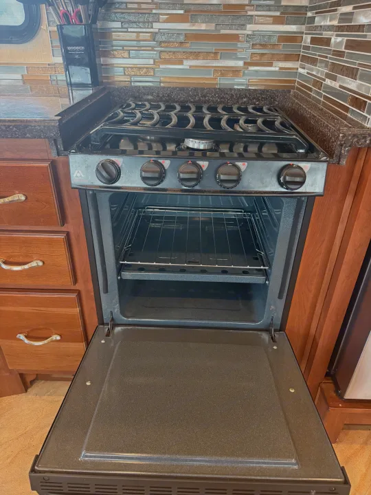 RV rental kitchen showing an open oven with racks and a stovetop with burners and controls. Ready for your cooking needs.. Fleetwood Bounder 2016