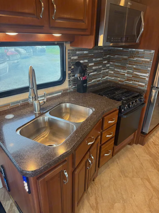This RV rental features a well-equipped kitchen with double stainless steel sink, gas stove, microwave, wood cabinets, and tiled backsplash.. Fleetwood Bounder 2016