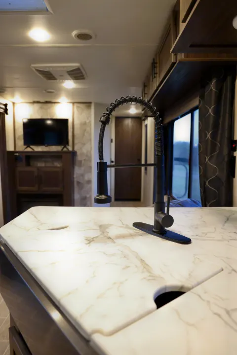 This rv rental features a modern kitchen with a sleek black faucet, marble-look countertop, and a cozy living area with TV.. Forest River Cherokee 2020