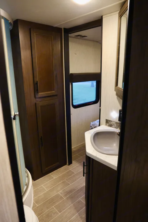 Tour a compact RV rental bathroom with dark wood cabinetry, a sink, shower, and toilet, perfect for travel.. Forest River Cherokee 2020