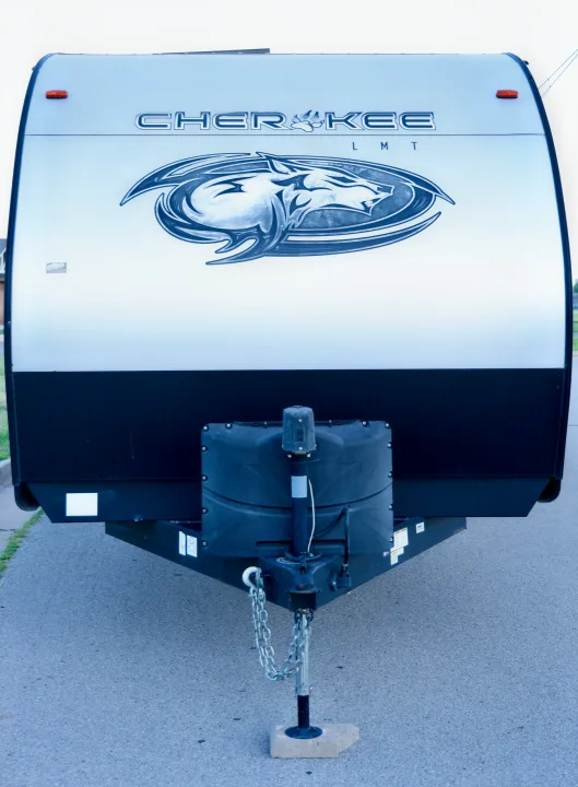 Front view of a silver Cherokee RV rental travel trailer with its iconic wolf emblem, propane tank cover, and hitch assembly.. Forest River Cherokee 2020
