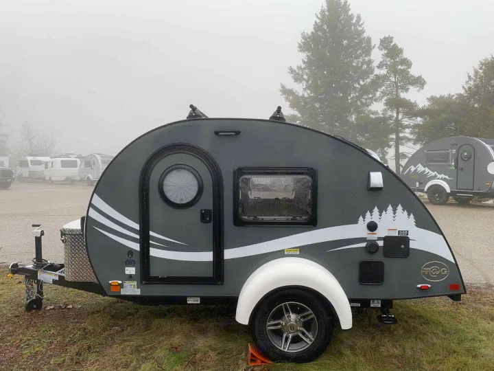 Explore in this sleek gray teardrop camper RV rental, featuring pine graphics, parked outdoors on a foggy day.. nuCamp T@G 2023