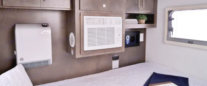 RV rental bedroom: a bed with white bedding, wall heater, AC unit, storage, and window provide comfort.. nuCamp T@G 2023