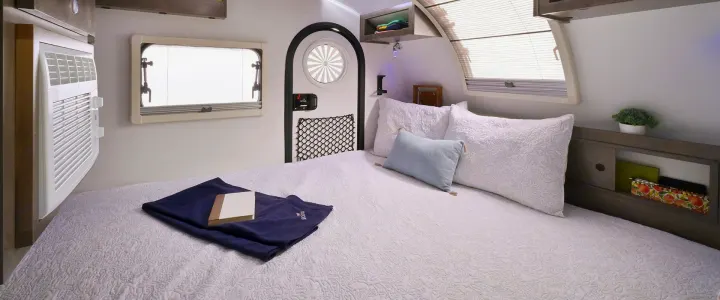 Experience comfort in this RV rental bedroom: AC, windows, arched door, cozy bed with textured quilt & storage.. nuCamp T@G 2023