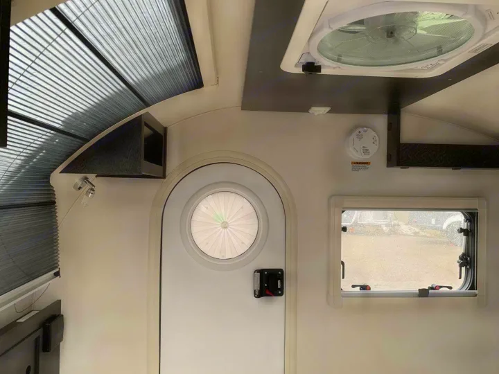 Bright rv rental interior with a ceiling fan, entry door, window, pleated shades, and a safety detector.. nuCamp T@G 2023