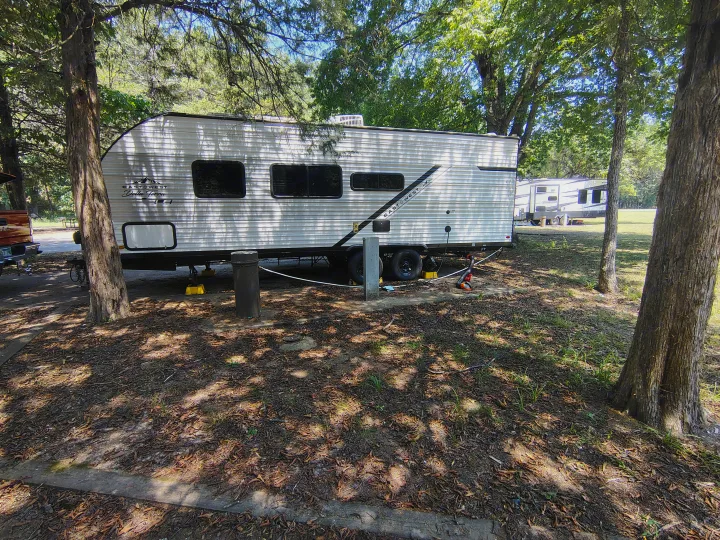 White travel trailer RV rental at a shaded campsite, connected to utilities for a relaxing stay amidst nature.. East to West Della Terra LE 2024