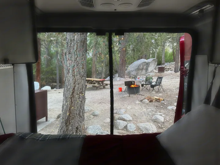 Cozy view from an RV rental, looking out at a peaceful campsite with a warm campfire, trees, and rocks. Perfect camping!. Winnebago Winnebago 2023