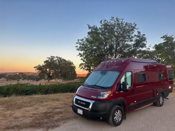 Red Winnebago Solis camper van rv rental at sunset, parked near a vineyard. Ideal for a scenic road trip.. Winnebago Winnebago 2023
