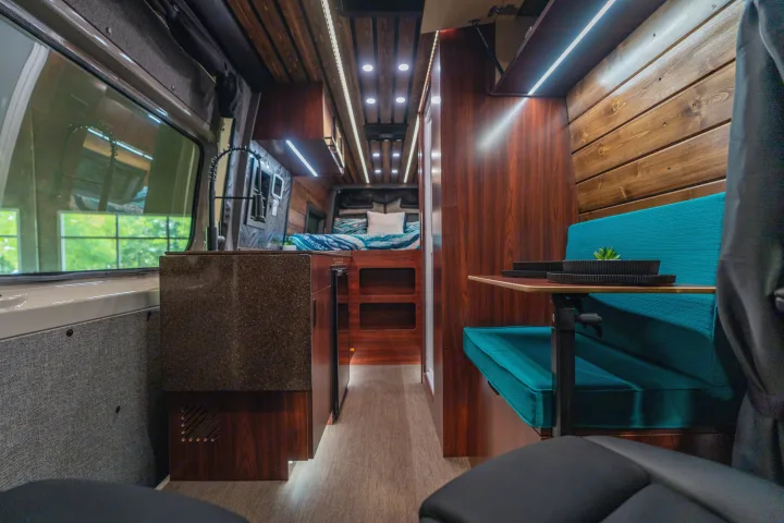 Modern RV rental interior: kitchen, dining, and bed areas with warm wood and bright lighting.. Mercedes-Benz Sprinter 2025