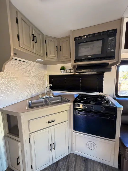 Modern RV rental kitchen: light gray cabinets, black microwave & stove, double sink, and geometric backsplash.. Coachmen Leprechaun 2002
