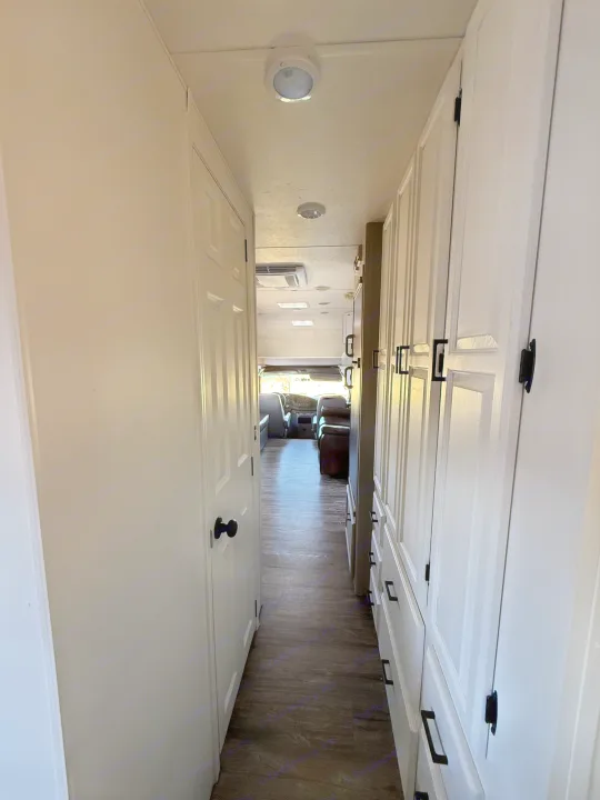 Step inside this RV rental, showcasing a clean interior hallway with white cabinets and a door, leading to the cockpit.. Coachmen Leprechaun 2002