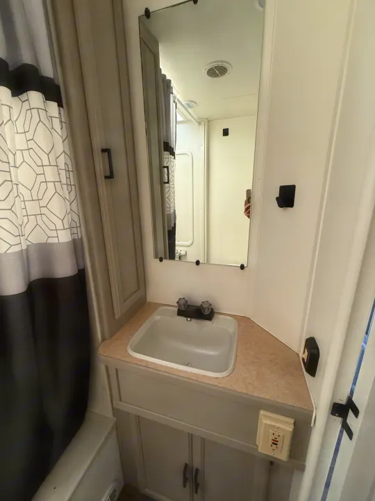 This RV rental bathroom features a compact sink, wall mirror, and a stylish black, gray, and white geometric shower curtain.. Coachmen Leprechaun 2002