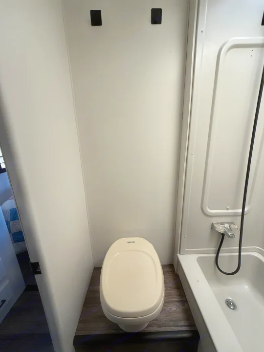 Compact rv rental bathroom with a beige toilet on wood-look flooring and a white shower/tub combo on the right.. Coachmen Leprechaun 2002