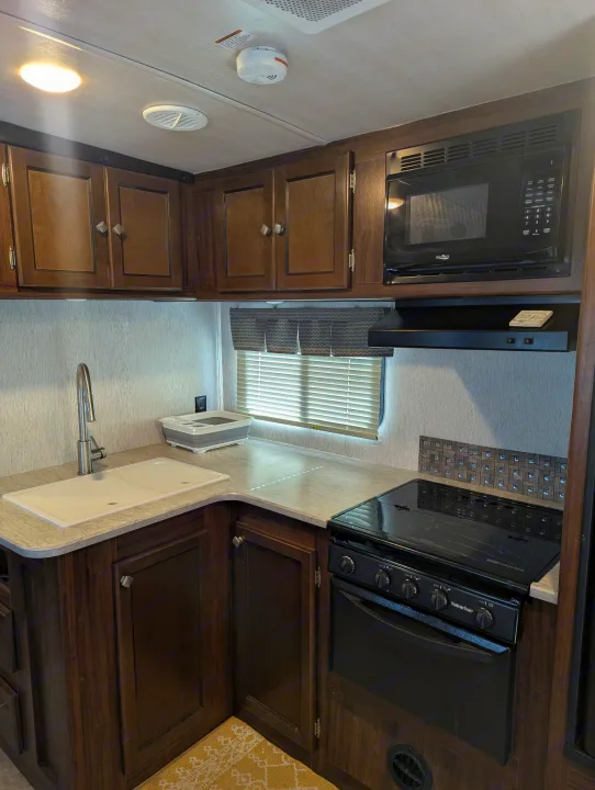 RV rental kitchen: dark wood cabinets, light counters, sink, microwave, and stove. Essential cooking amenities for travel.. Heartland RVs Wilderness 2018