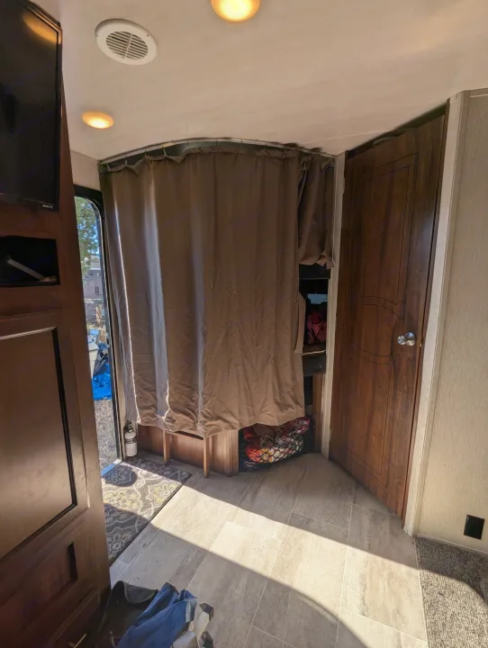 Step inside this RV rental: a cozy living area with a brown privacy curtain, light wood-look floor, and open door revealing outside.. Heartland RVs Wilderness 2018