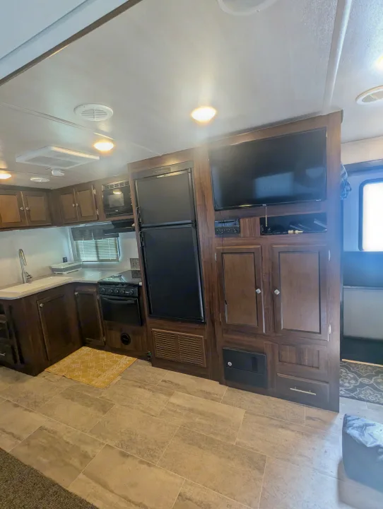 Full view of a modern RV rental interior featuring a compact kitchen, TV, fridge, and stylish cabinetry.. Heartland RVs Wilderness 2018