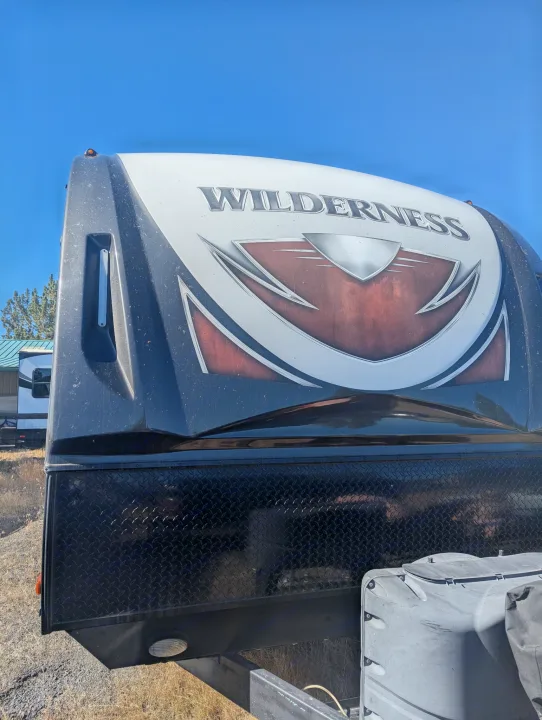 Front view of a Wilderness RV, ideal for an rv rental adventure. Note the brand logo, diamond plate, and covered propane tanks.. Heartland RVs Wilderness 2018
