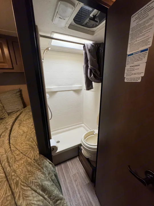 Compact RV rental interior features a bed, bathroom with shower, and toilet, with notices on the door.. Thor Majestic 2018