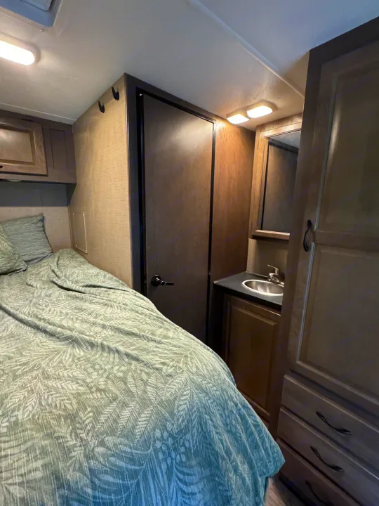 Inside an RV rental: Bed with leafy bedding, compact sink/vanity, and storage optimize small space.. Thor Majestic 2018