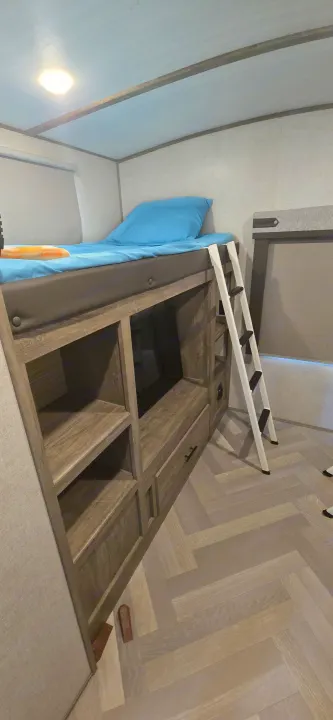 This RV rental offers a cozy bunk bed with blue linens, a white ladder, and ample built-in storage. Light herringbone flooring.. Forest River Salem Hemisphere 2021
