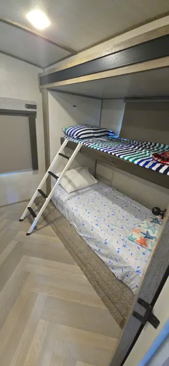 RV rental bunk beds: top with striped bedding, bottom with sea-themed sheets. A ladder provides access. Cozy interior for travel.. Forest River Salem Hemisphere 2021