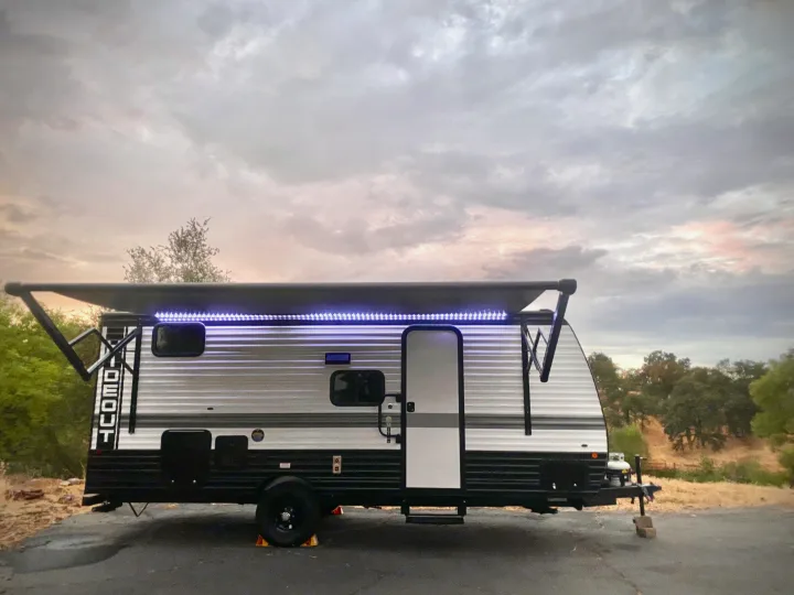 A modern travel trailer RV rental, branded 'Hideout', with an extended awning and blue LED lights, parked outdoors at dusk.. Keystone RV Hideout Sport 2024