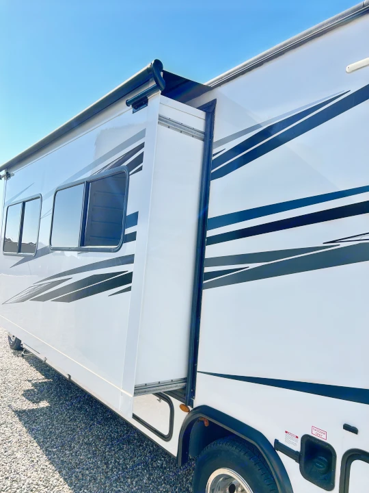 White RV rental with a side slide-out extended, showing its exterior design, windows, and road wheels on gravel.. Forest River Sunseeker LE 2022