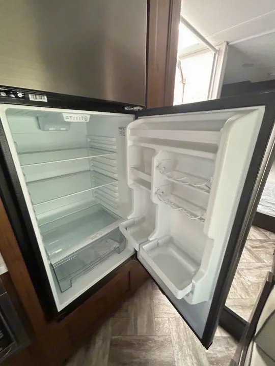 Empty and clean refrigerator in an RV rental, featuring interior shelves and door storage, ready for travel supplies.. Forest River Sunseeker LE 2022
