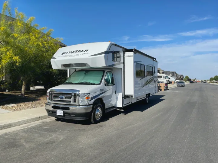 A white Sunseeker Class C RV rental is parked on a residential street on a sunny day, ready for your next travel adventure!. Forest River Sunseeker LE 2022