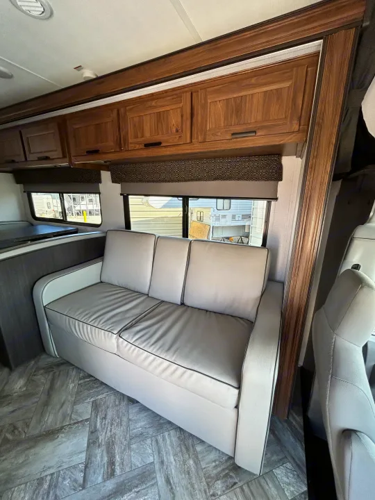 Inside an RV rental: a light gray sofa, wood cabinets, and large windows overlooking the outside. Herringbone flooring adds style.. Forest River Sunseeker LE 2022