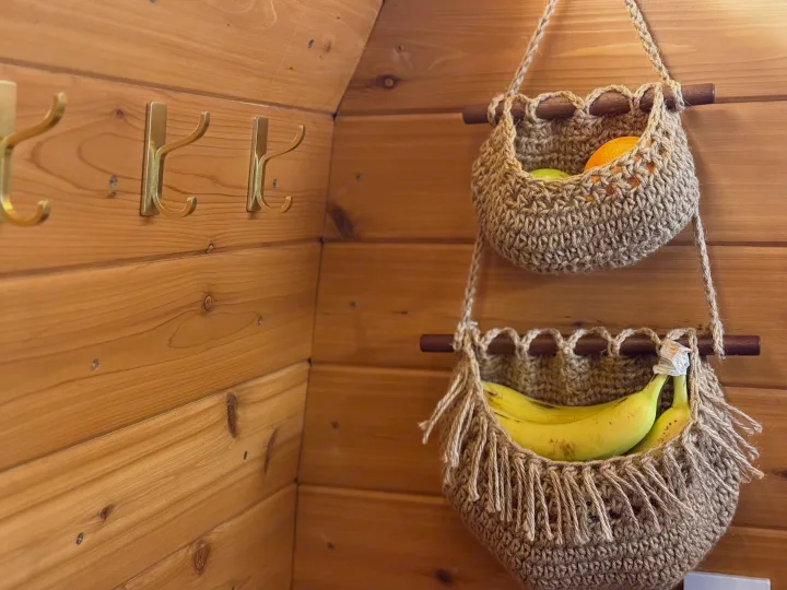 Cozy rv rental interior: wooden walls, brass hooks, and two crocheted baskets holding fruit. Organized storage for your travels.. RAM Promaster 2500 2020