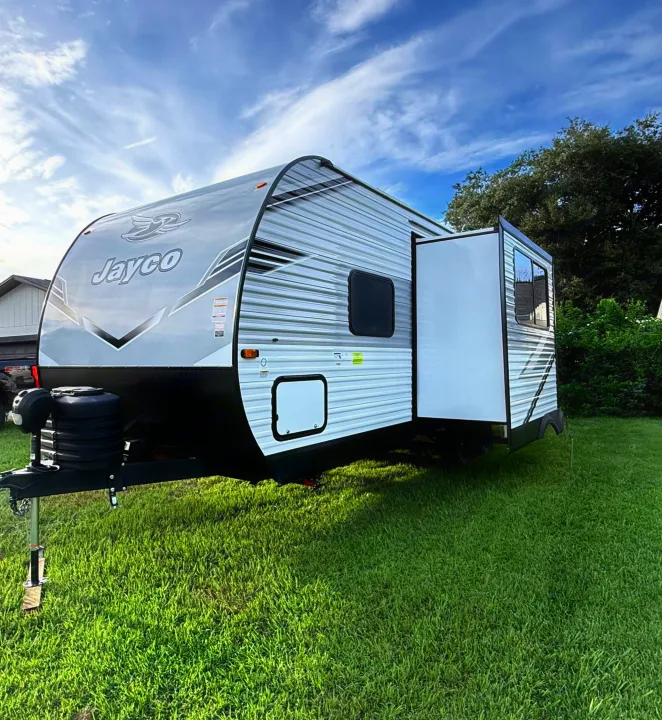 A Jayco travel trailer with an extended slide-out is parked on a green lawn with a truck nearby, great for an rv rental.. jayco 235MBH Jay Flight TT 2025