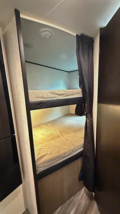 Interior view of an RV rental showing stacked bunk beds with mattresses & privacy curtain for comfortable sleeping.. jayco 235MBH Jay Flight TT 2025