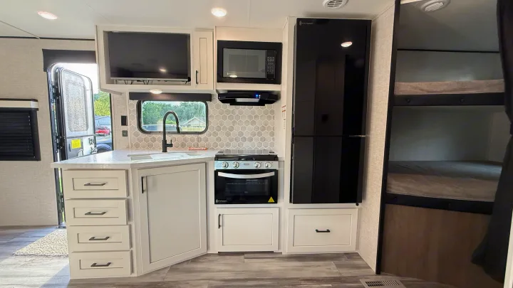 Modern RV rental interior showcasing a bright kitchen with oven, microwave, large fridge, TV, and bunk beds.. jayco 235MBH Jay Flight TT 2025