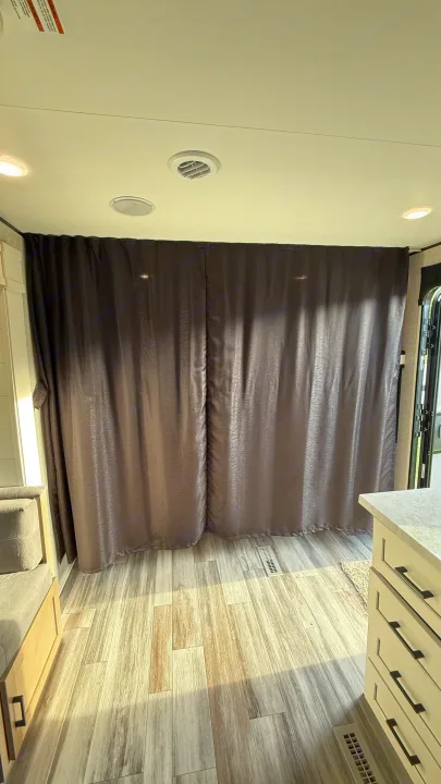 Dark gray curtains create a private space in this RV rental's interior, featuring wood-look flooring and modern cabinetry.. jayco 235MBH Jay Flight TT 2025