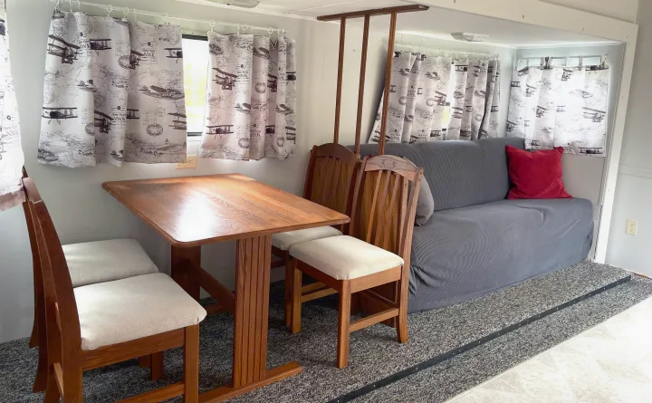 Inside an RV rental, showing a dining table with chairs, a gray sofa, and airplane-themed curtains.. Jayco Eagle 1998