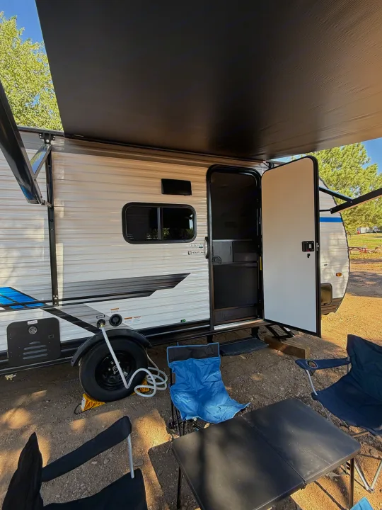 Enjoying the outdoors with an RV rental. A travel trailer, extended awning, camping chairs, and table set up at a sunny campsite.. Heartland RVs Pioneer 2025
