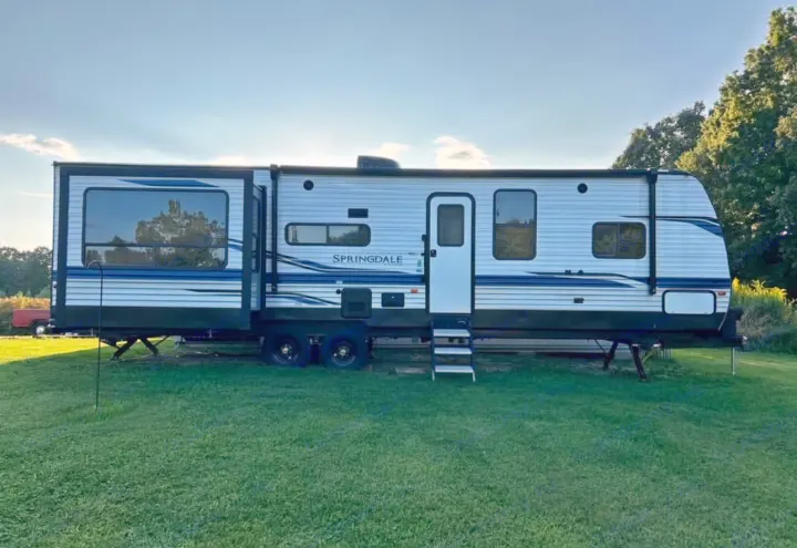 This Springdale RV rental, a white travel trailer with blue stripes, is parked on green grass under a blue sky.. Keystone RV Springdale 2022